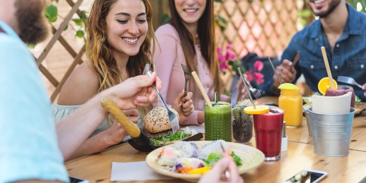 Happy friends lunching with healthy food in bar coffee brunch - Young people having fun eating meal and drinking smoothies fresh fruits in rustic restaurant - Health nutrition lifestyle concept