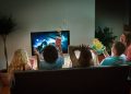 Group of young people in suspense watching a scary movie on TV together at home for Halloween. Image on TV screen is photographer's own.