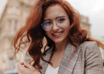 Pretty woman in eyeglasses and jacket looking into camera