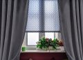 Home window with a patterned blind and black curtains.