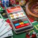 Casino online. Smartphone or mobile phone, slot machine, dice, cards and roulette on a green table in casino. 3d illustration