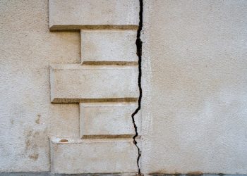 A huge crack in the rough textured surface of a plastered wall, background. Backdrop or graphic resource for design.